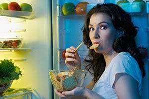 woman eating in front of open fridge
