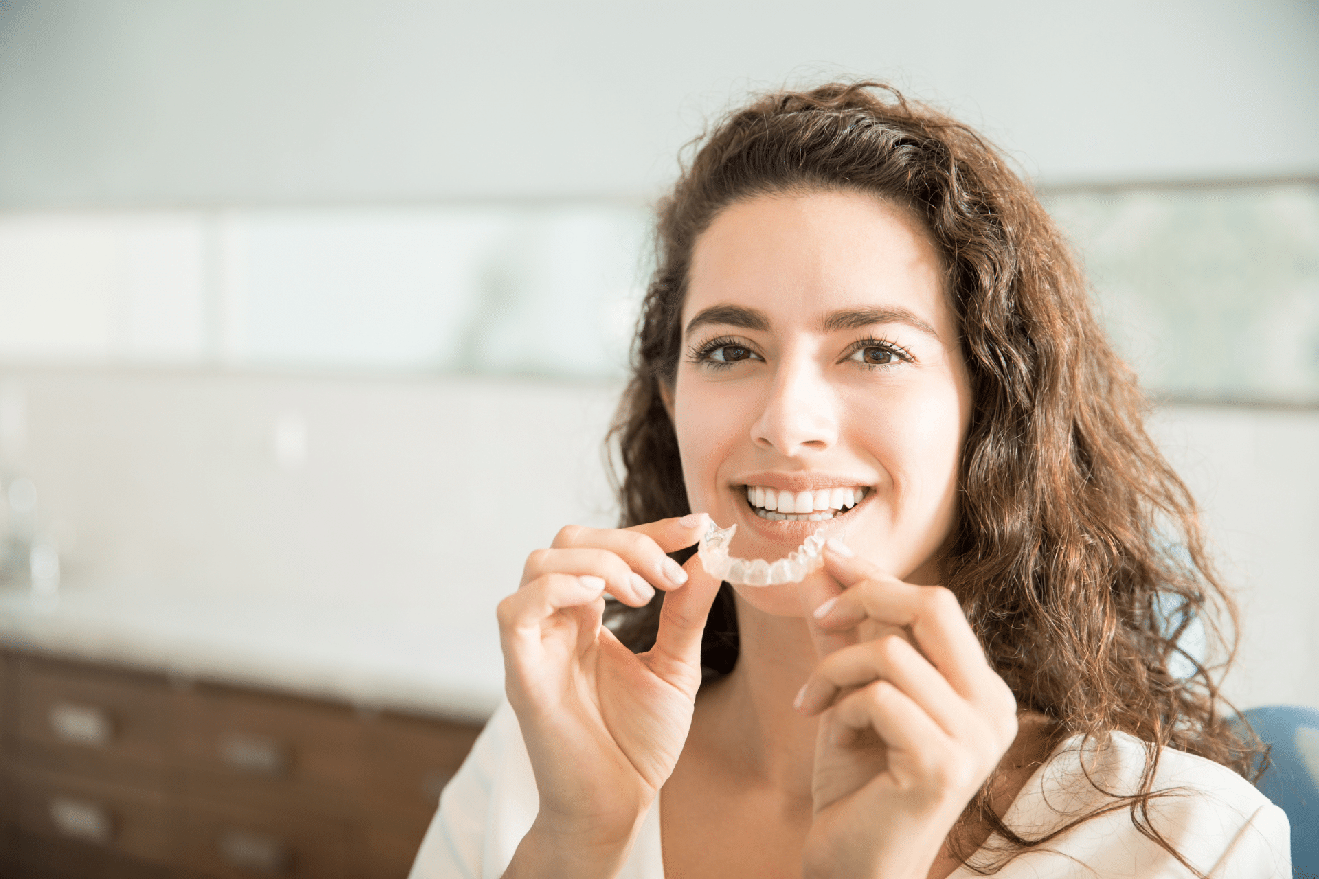 Smiling adult woman holding a clear aligner near her teeth