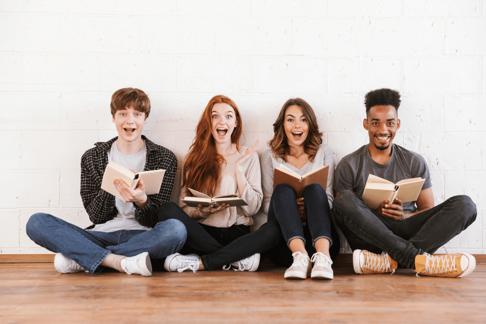 Four smiling college students sitting together and holding open books.