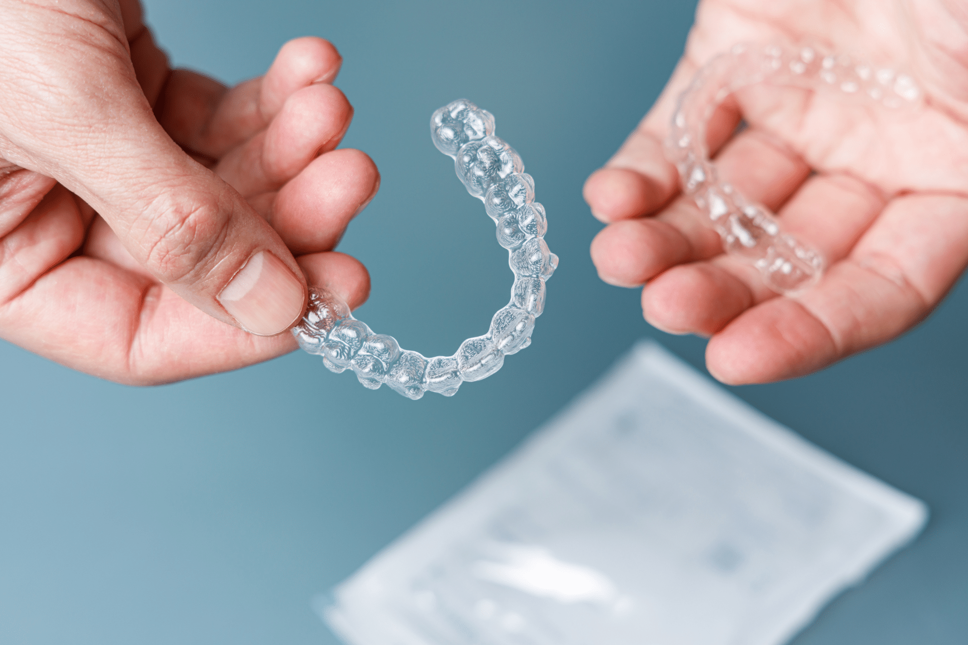 Close-up of hands holding upper and lower clear dental aligners.